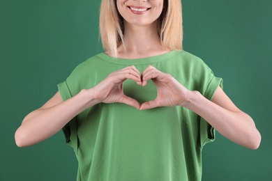 Woman making heart with her hands on color background, closeup