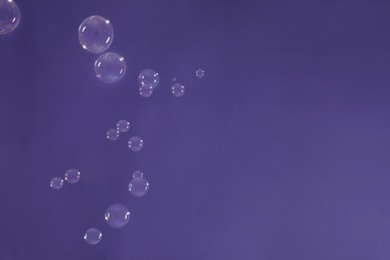 Photo of Many beautiful soap bubbles on purple background. Space for text