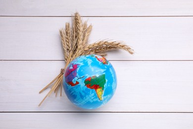 Photo of Globe and ears of wheat on white wooden table, flat lay. Import and export concept