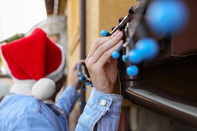 Photo of Man in Santa hat decorating house with Christmas lights outdoors, selective focus