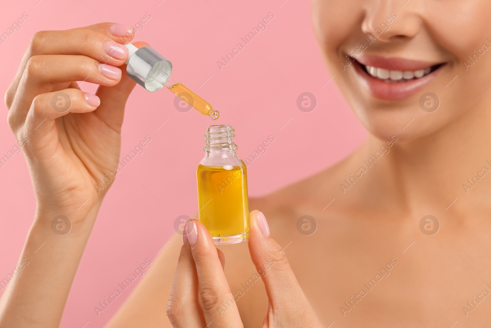 Photo of Young woman with serum in her hands on pink background, closeup