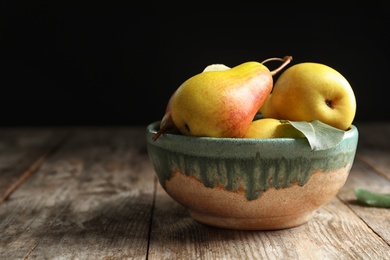 Photo of Bowl with ripe pears on wooden table against dark background. Space for text