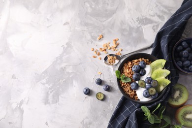 Tasty granola with yogurt, blueberries and kiwi in bowl on gray textured table, flat lay. Space for text