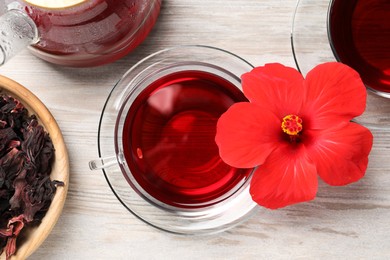 Photo of Delicious hibiscus tea and beautiful flower on light wooden table, flat lay