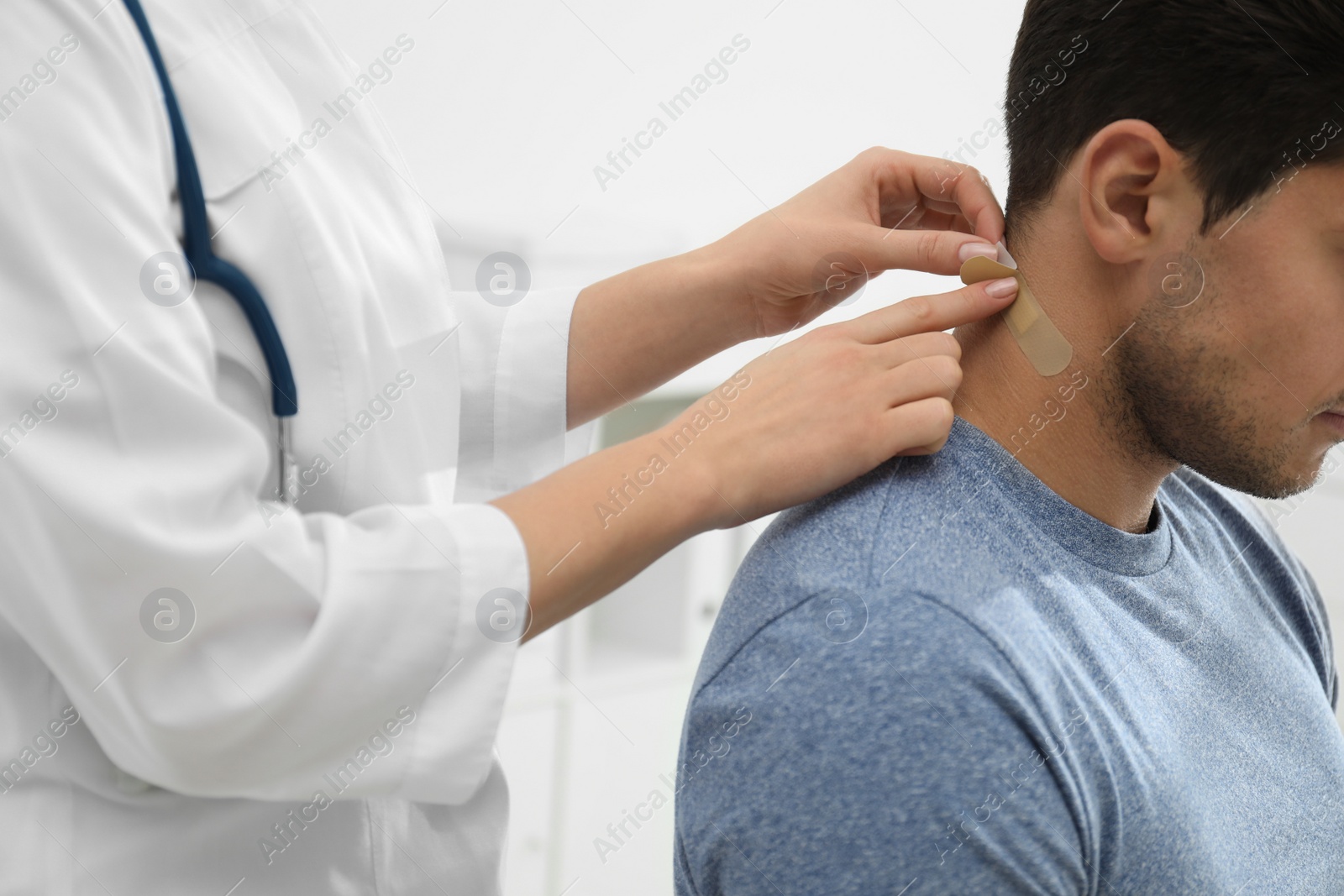 Photo of Doctor putting sticking plaster onto man's neck indoors, closeup