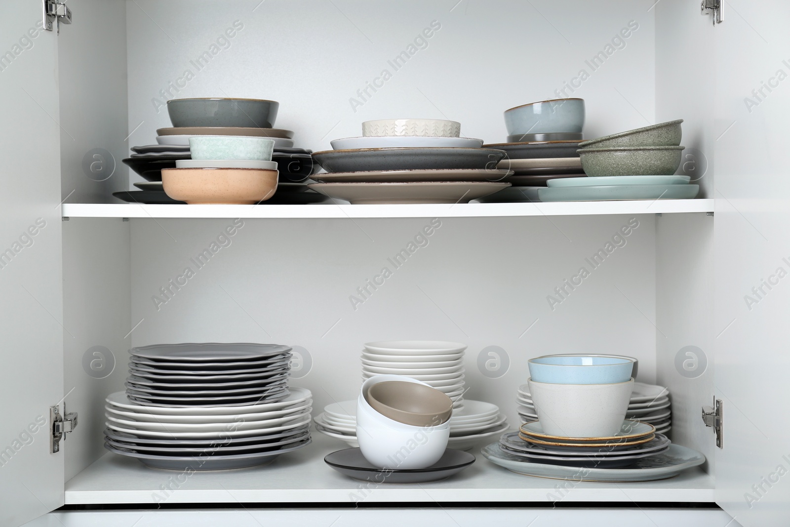 Photo of Different clean plates and bowls on shelves in cabinet