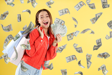 Image of Happy young woman with dollars under money rain on yellow background