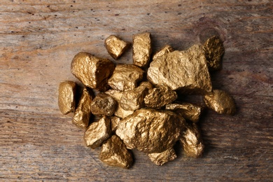 Photo of Pile of gold nuggets on wooden background, top view