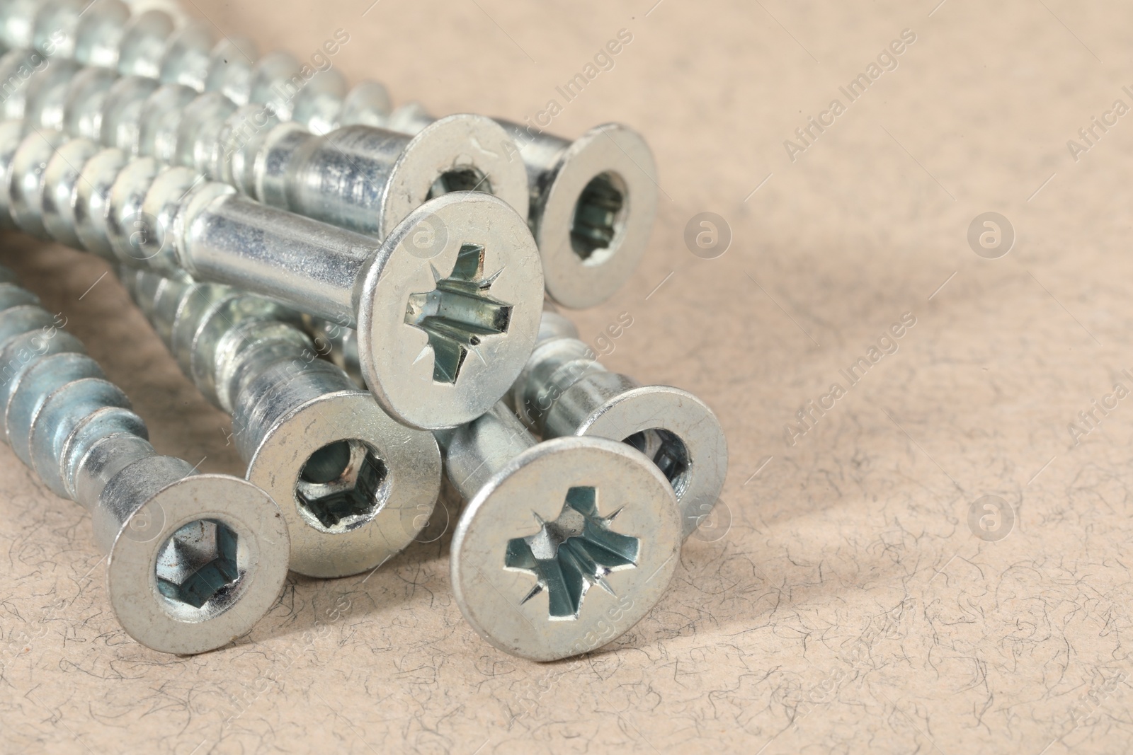 Photo of Many metal screws on beige background, closeup. Space for text