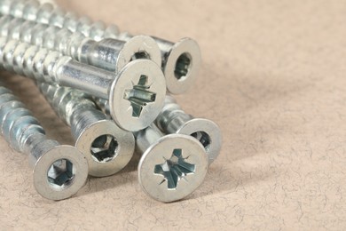 Many metal screws on beige background, closeup. Space for text