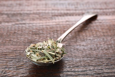 Photo of Metal spoon with aromatic dried lemongrass on wooden table