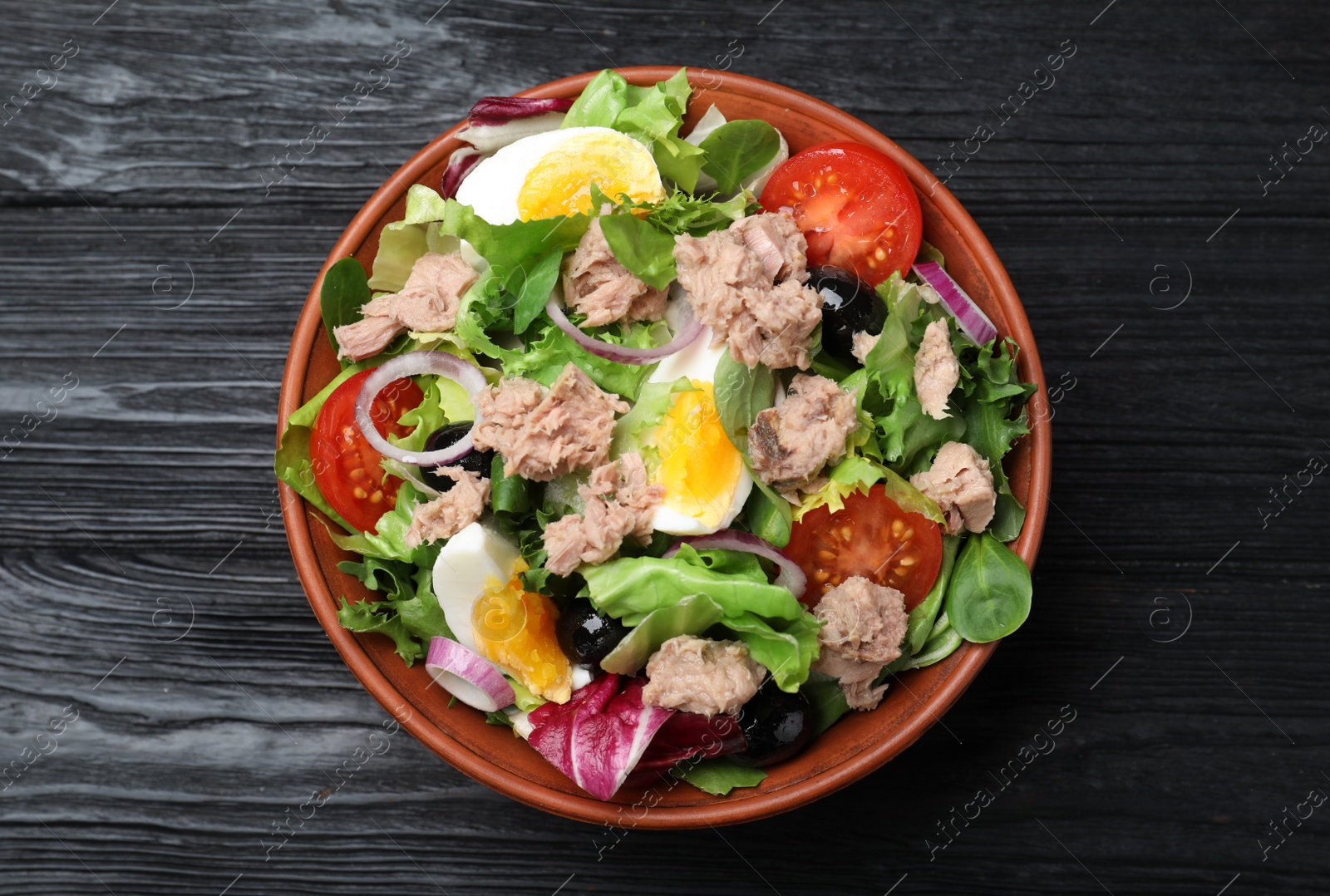 Photo of Bowl of delicious salad with canned tuna and vegetables on black wooden table, top view