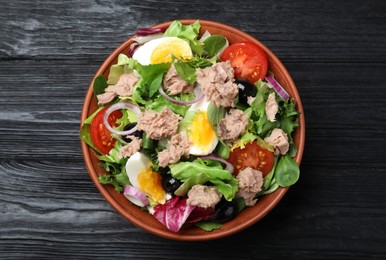 Photo of Bowl of delicious salad with canned tuna and vegetables on black wooden table, top view