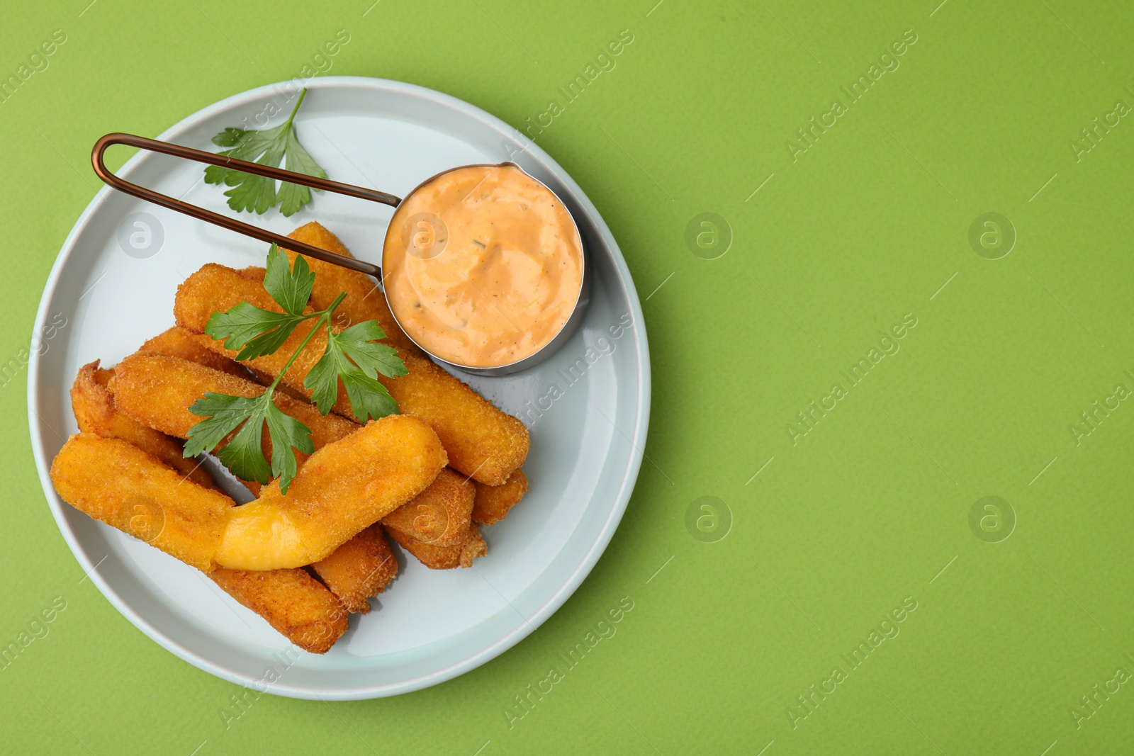 Photo of Tasty fried mozzarella sticks served with sauce and parsley on green background, top view. Space for text