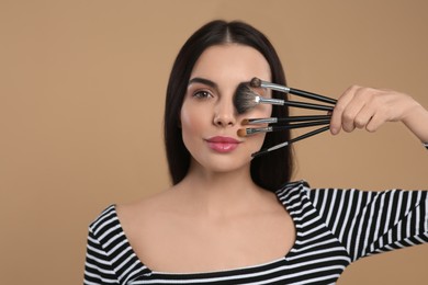 Beautiful woman with different makeup brushes on light brown background