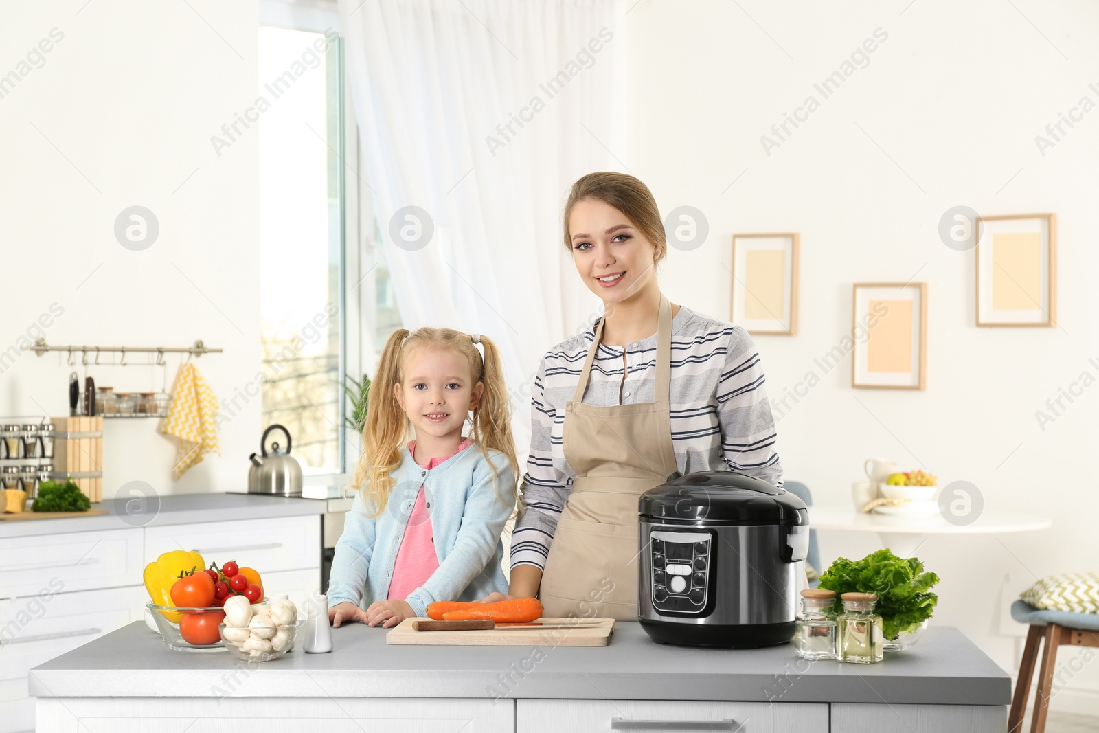 Photo of Mother and daughter preparing food with modern multi cooker in kitchen