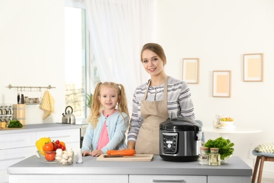 Mother and daughter preparing food with modern multi cooker in kitchen