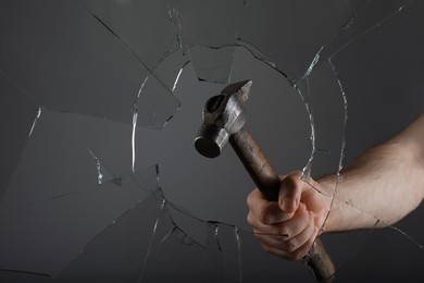 Man breaking window with hammer on grey background, closeup