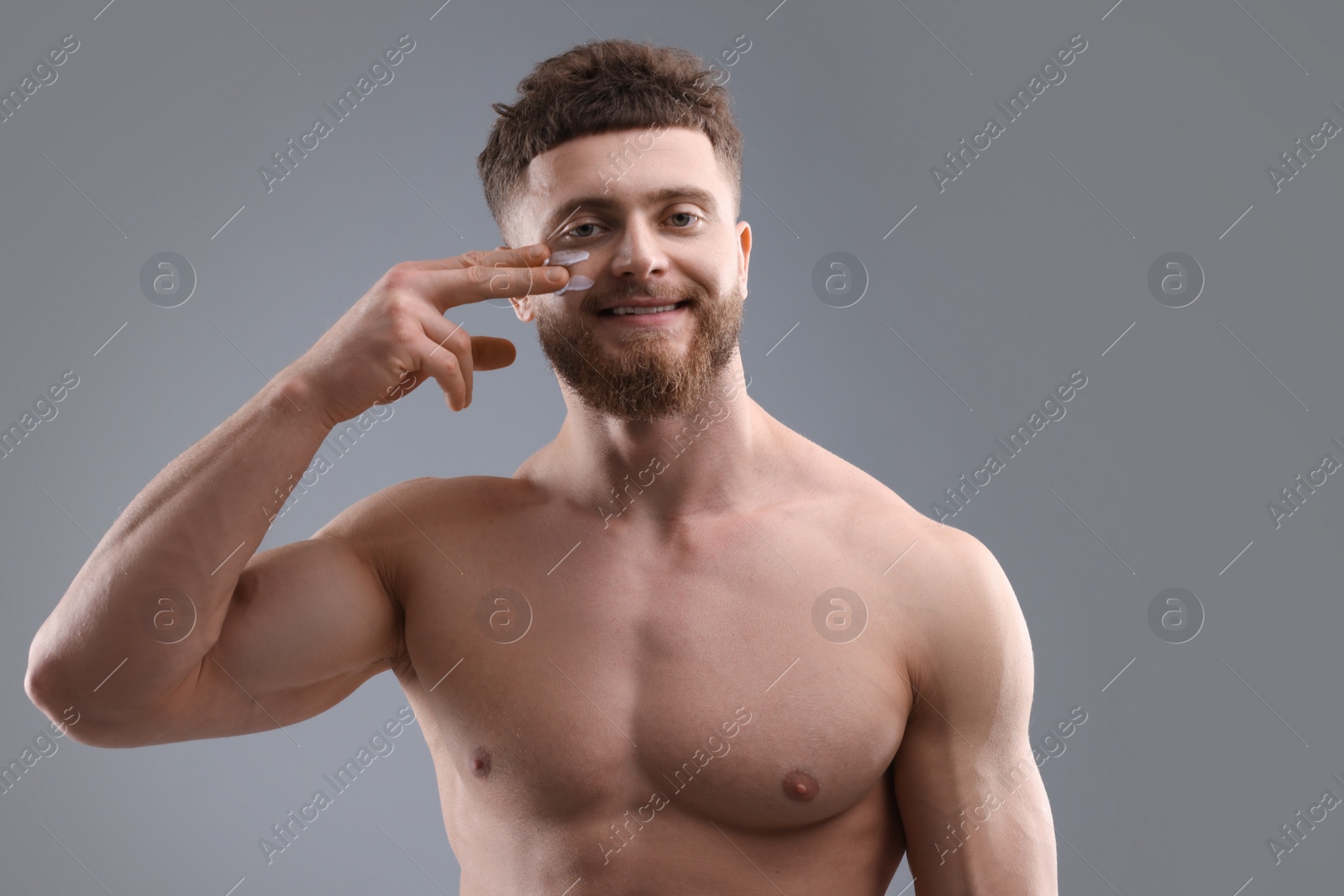 Photo of Handsome man applying moisturizing cream onto his face on grey background