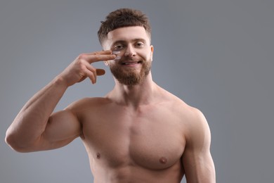 Handsome man applying moisturizing cream onto his face on grey background