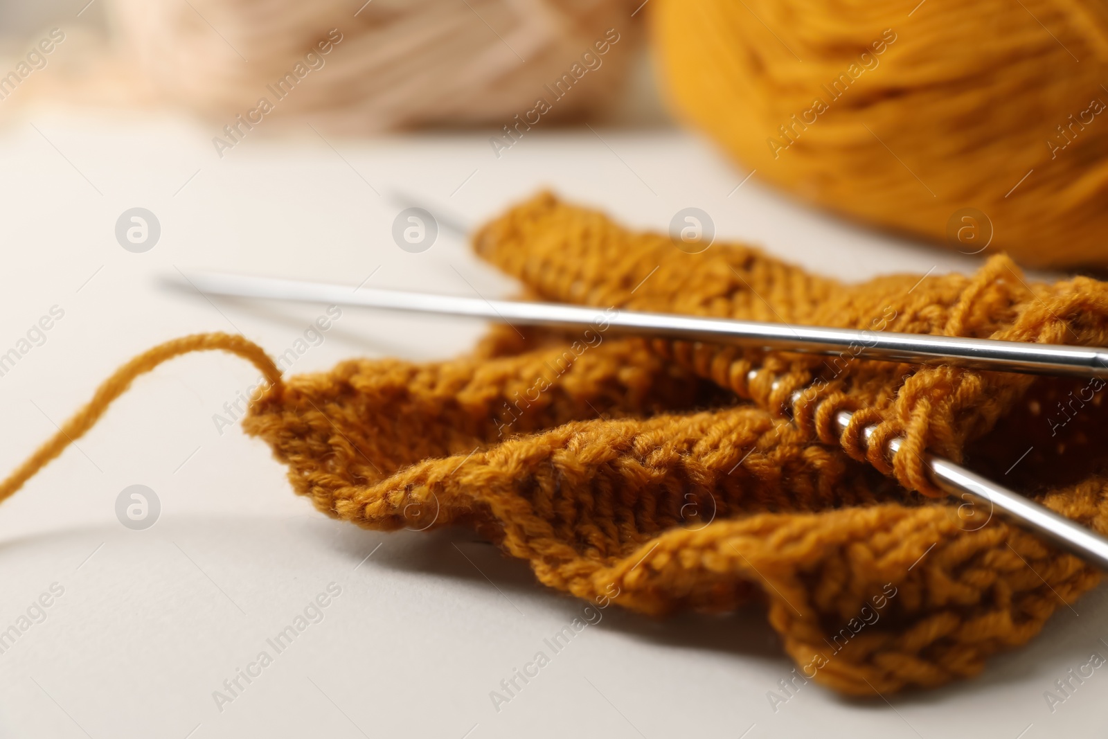 Photo of Soft orange knitting and metal needles on beige background, closeup