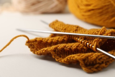 Soft orange knitting and metal needles on beige background, closeup