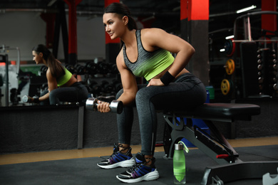 Photo of Young woman working out with dumbbell in modern gym