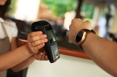 Photo of Man using terminal for contactless payment with smart watch in cafe, closeup