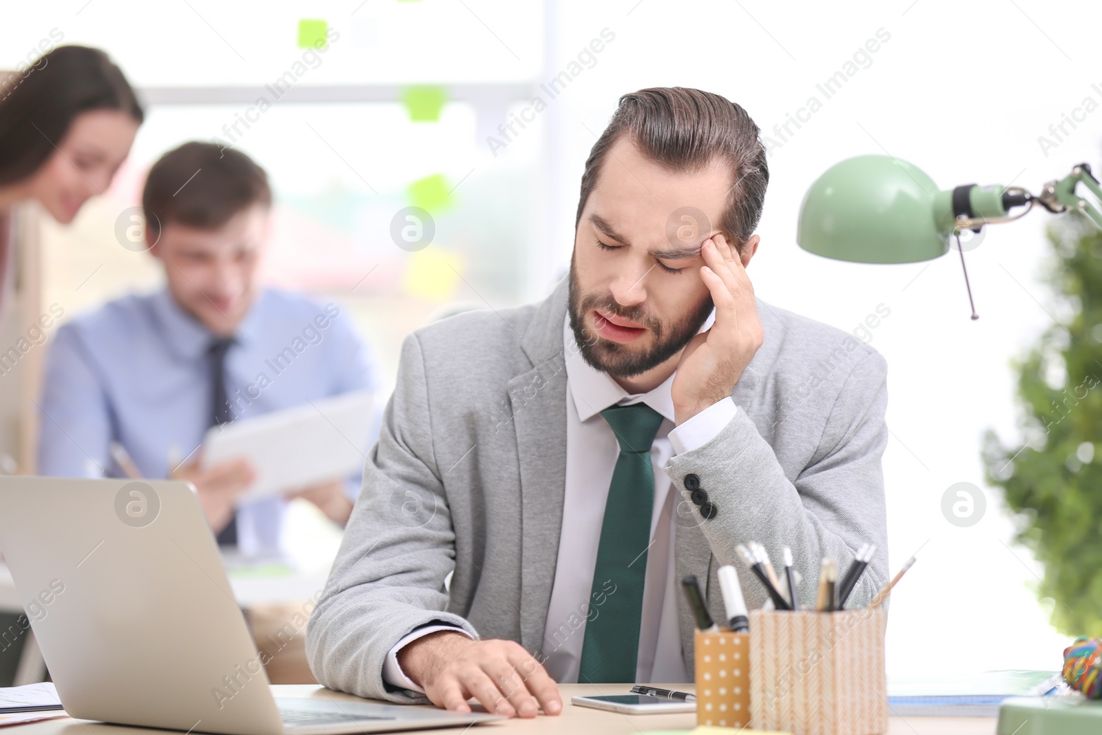 Photo of Young man suffering from headache in office