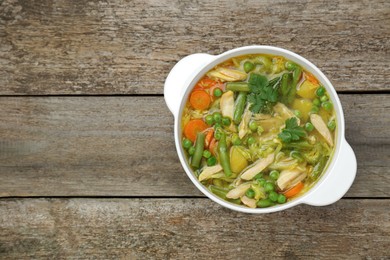 Photo of Saucepan of delicious vegetable soup with chicken on wooden table, top view. Space for text