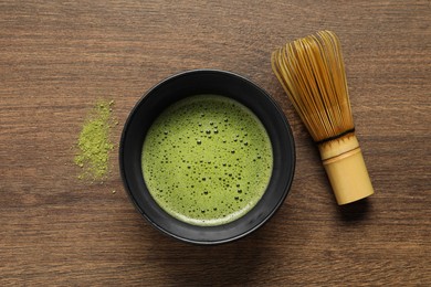 Cup of fresh matcha tea, green powder and bamboo whisk on wooden table, flat lay