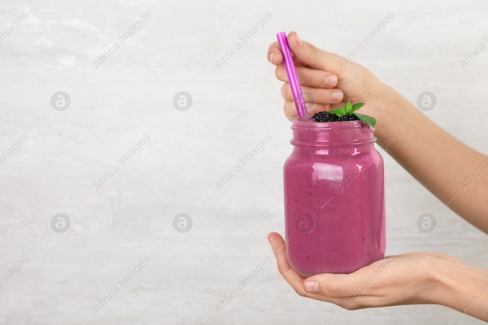 Photo of Young woman holding mason jar of tasty blackberry smoothie on light grey background, closeup. Space for text