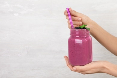 Young woman holding mason jar of tasty blackberry smoothie on light grey background, closeup. Space for text