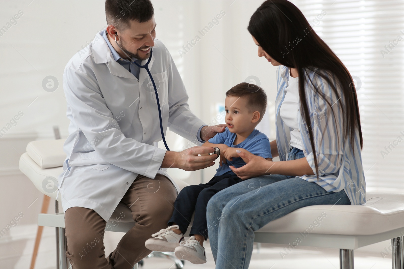 Photo of Mother and son visiting pediatrician in hospital. Doctor examining little boy