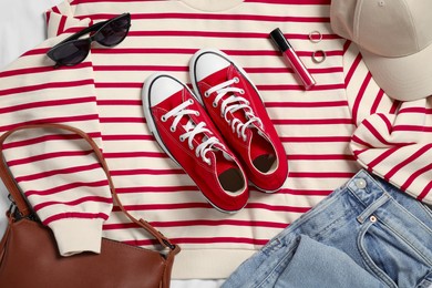 Photo of Pair of stylish red sneakers, clothes and accessories on white fabric, flat lay