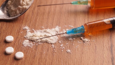 Pills, syringes and powder on wooden table, closeup. Hard drugs