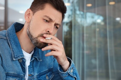 Photo of Handsome man smoking cigarette outdoors. Space for text