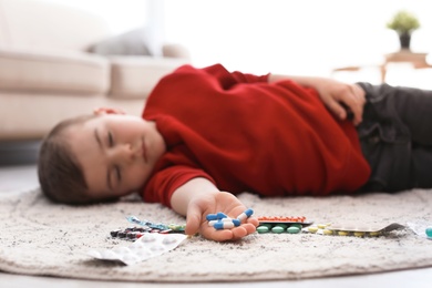 Photo of Unconscious little child with pills lying on floor at home. Household danger