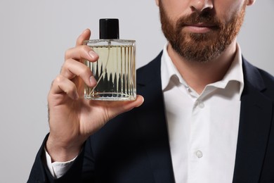 Photo of Handsome bearded man with bottleperfume on light grey background, closeup