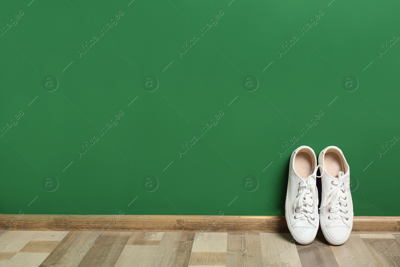 Photo of Stylish sneakers on floor near color wall, space for text