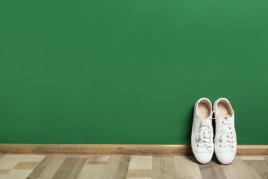 Stylish sneakers on floor near color wall, space for text