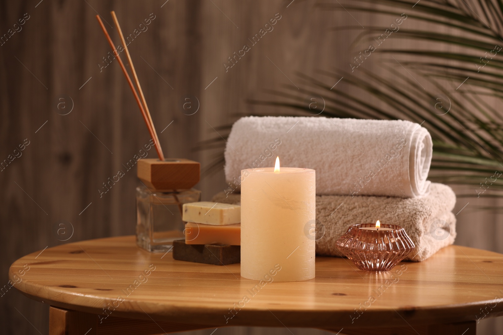 Photo of Spa composition. Burning candles, towels, soap and reed air freshener on wooden table, closeup