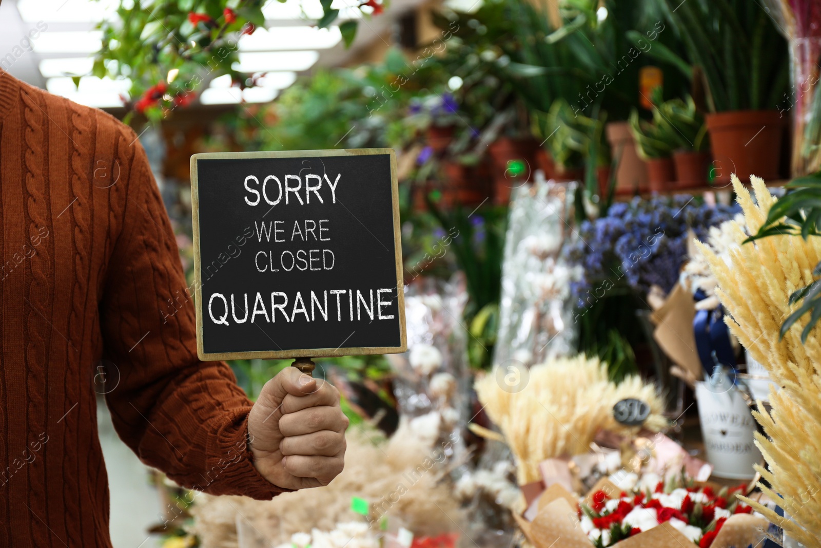 Image of Business owner holding sign with text SORRY WE ARE CLOSED QUARANTINE in flower shop, closeup