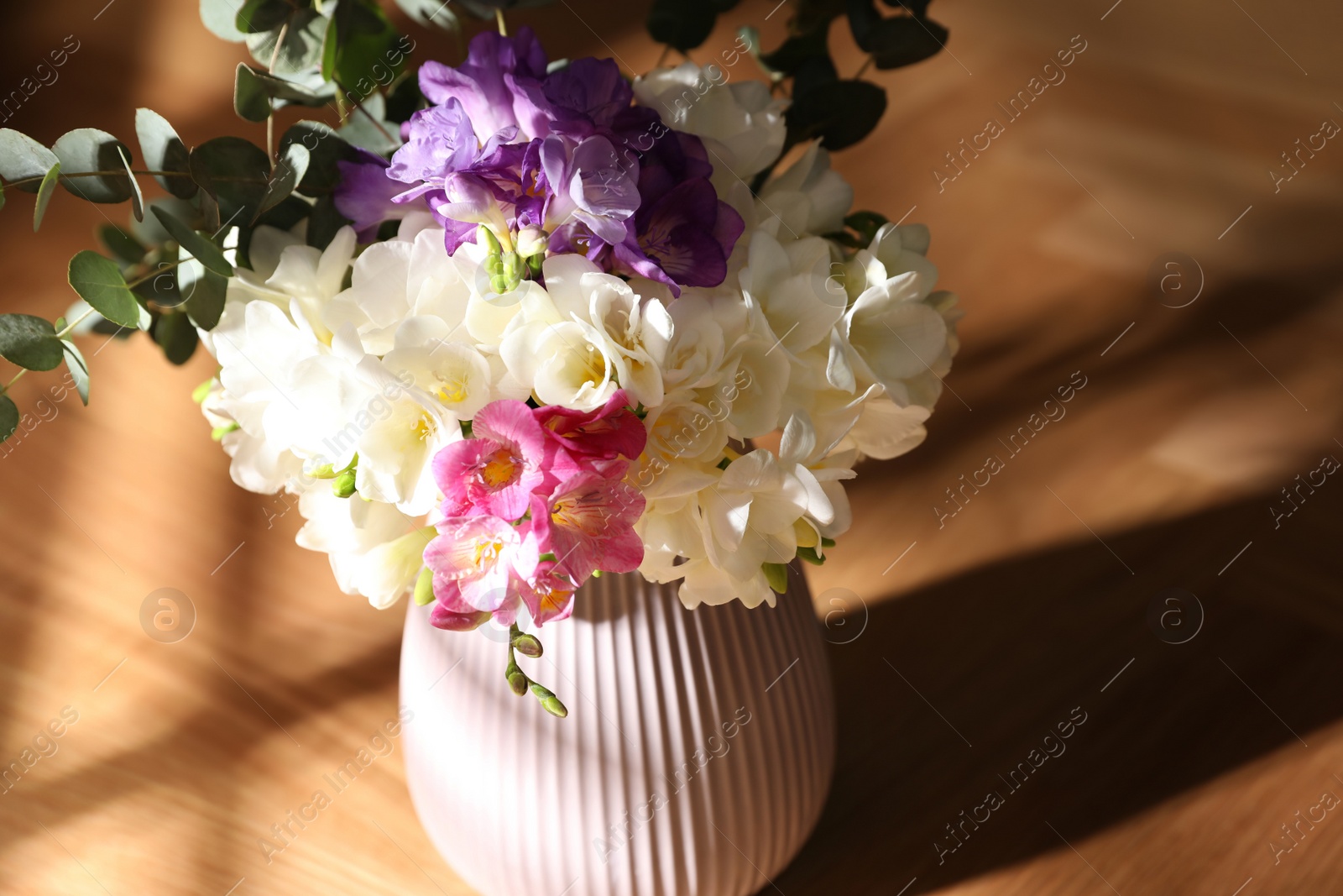 Photo of Beautiful bouquet with spring freesia flowers on sunlit wooden table in room, closeup