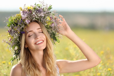 Young woman wearing wreath made of beautiful flowers in field on sunny day