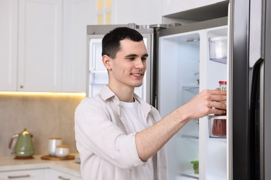 Photo of Happy man taking sauce out of refrigerator in kitchen