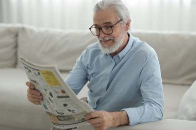 Portrait of grandpa with stylish glasses reading newspaper on sofa indoors