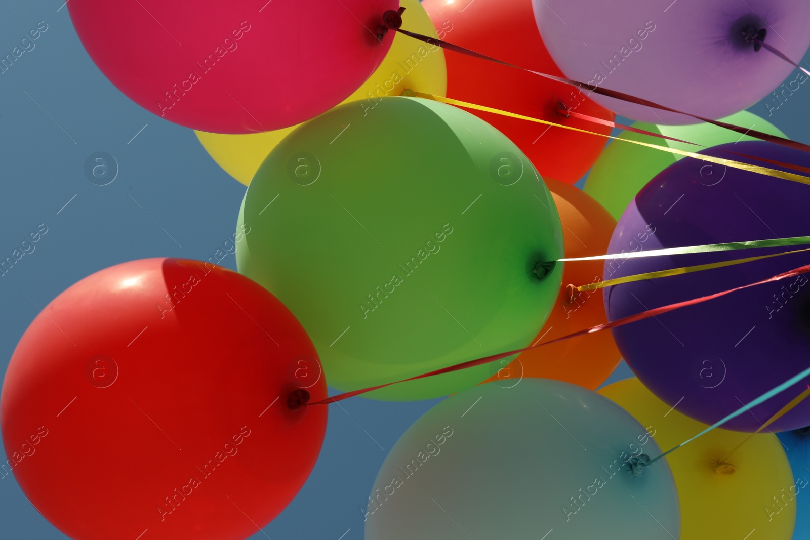 Photo of Bunch of colorful balloons against blue sky, bottom view