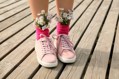 Woman with beautiful tender flowers in socks on wooden pier, closeup