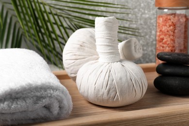 Photo of Herbal massage bags, rolled towel, spa stones and sea salt on wooden tray, closeup